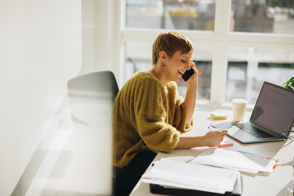 Smiling businesswoman making notes while talking on phone. Female executive working at her desk.